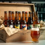 An open craft beer subscription box with assorted beer bottles and a tasting glass on a kitchen counter, shot in a warm editorial style.